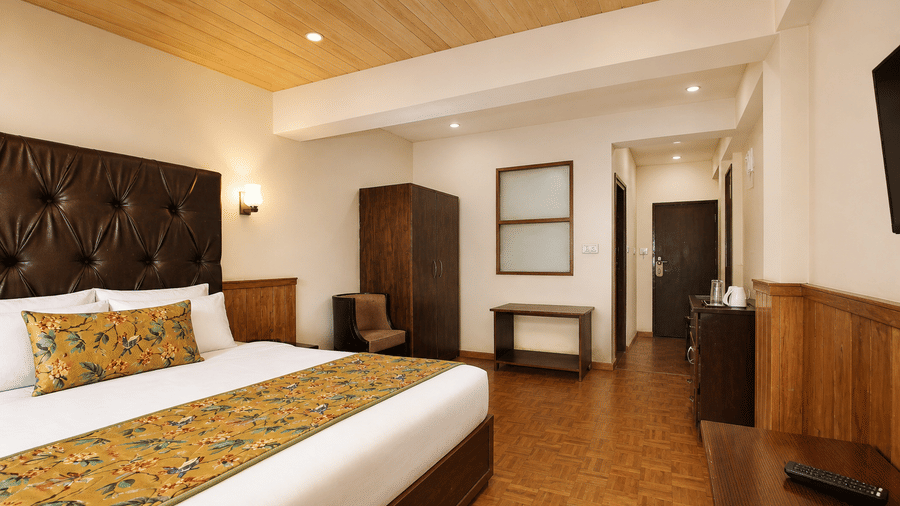 Deluxe Room at Orsino Khangri Karpo Retreat & Spa, Lachung, featuring a large bed and dark wooden furniture. 
