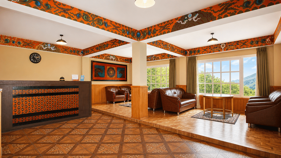 The reception area of Orsino Khangri Karpo Retreat & Spa, Lachung showing a wooden desk, tiled flooring, and a seating area with sofas near a window.