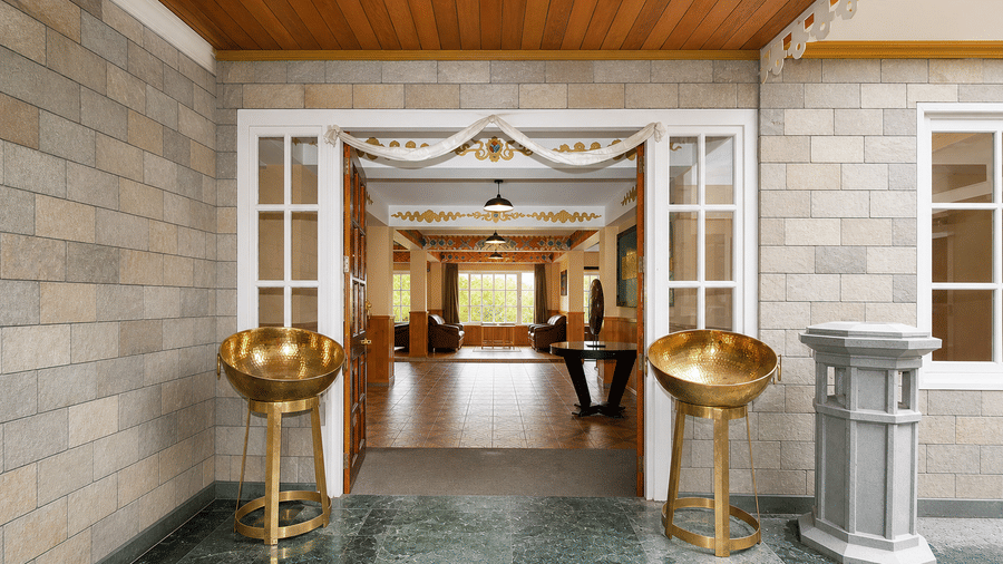 The entrance of Orsino Khangri Karpo Retreat & Spa, Lachung with stone walls and glass doors flanked by metal stands and a pillar.