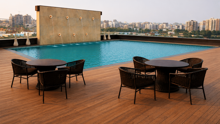 Rooftop dining next to the swimming pool at The Empresa Hotel with a fountain feature wall and wicker table-and-chair sets on a wooden deck, city skyline beyond.