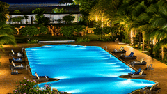 Swimming pool beautifully illuminated at night with lounge chairs and palm trees at Chariot Beach Resort, offering a magical evening setting.