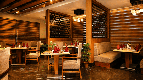 Restaurant seating area with wooden dining tables and chairs, a wooden lattice partition, exposed wooden beam ceiling and dark polished flooring.