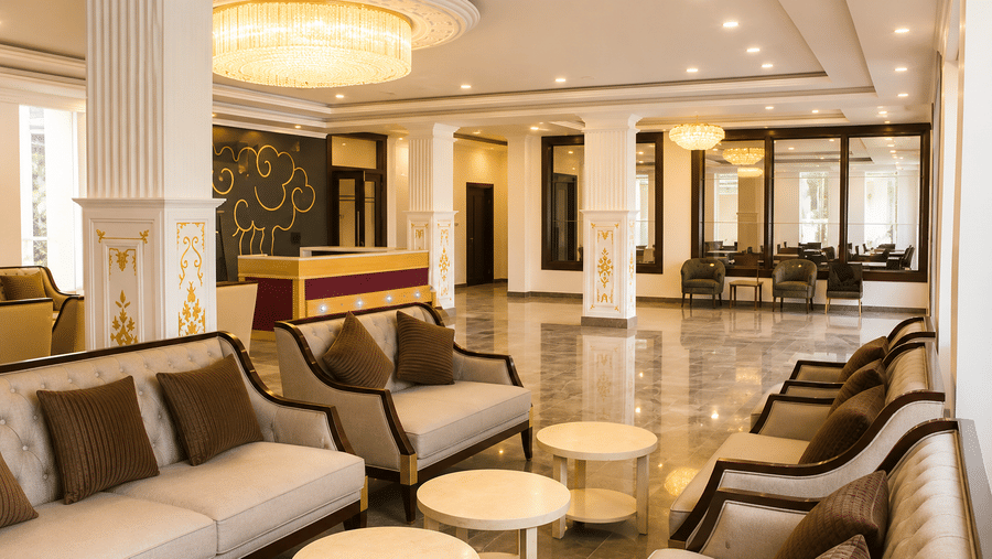 Hotel lobby seating area with beige sofas and armchairs, round side tables, marble pillars and a domed ceiling with warm lighting overhead.