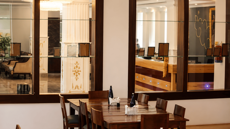 Restaurant seating area with wooden tables and chairs, a wall-mounted chandelier, glass panelling and warm ambient lighting throughout it.