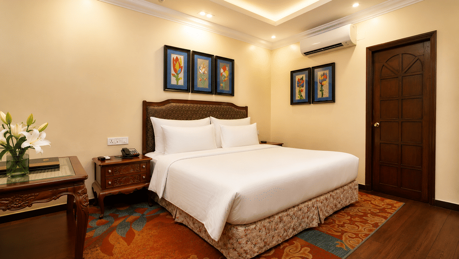 Executive room with a king bed, upholstered headboard, framed floral prints, bedside telephone, writing desk and a patterned carpet at MAYFAIR Garden, Rourkela.