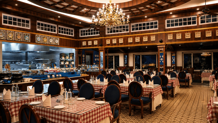 Tiffany restaurant with red-and-white chequered tablecloths, blue high-back chairs, an open live kitchen and a chandelier at MAYFAIR Himalayan Spa Resort, Kalimpong.