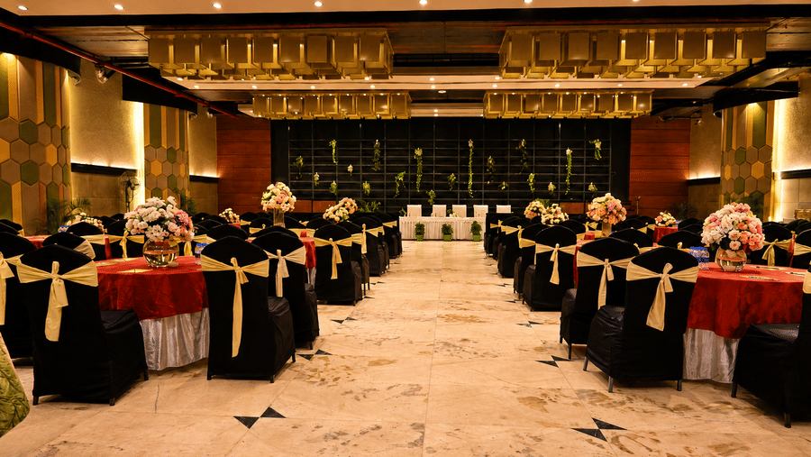 Banquet hall with round tables dressed in black and red linen with gold sashes, a floral stage backdrop and polished marble flooring throughout.