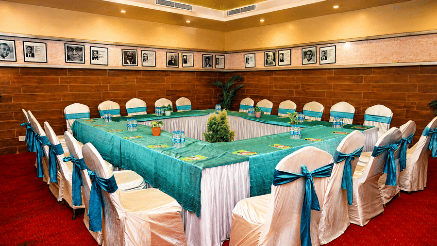 Boardroom set up with a U-shaped table dressed in teal cloth, white chair covers with teal sashes, a red carpet and framed photos on the wall.
