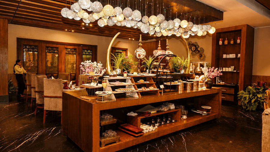 Restaurant buffet counter with a wooden display unit, a floral decor arrangement overhead and dining tables set out neatly in the background.