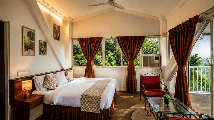 Sunlit bedroom at Wind Chalet with vaulted ceiling, king double bed, red lounge chairs, and balcony view outside.