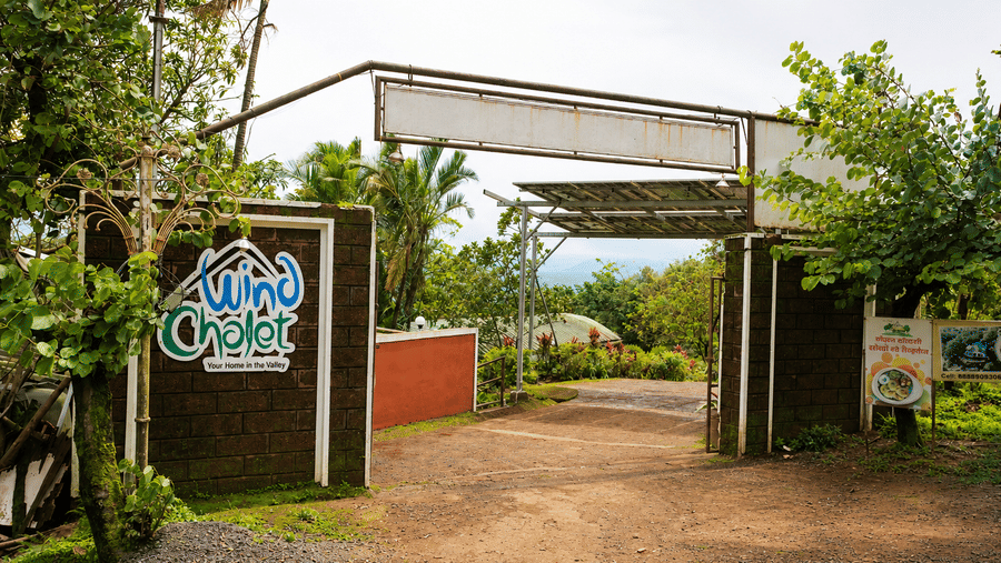 Entrance archway to Wind Chalet property featuring a branded logo sign, open driveway, and surrounding foliage.