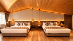 A hotel room with two beds side-by-side, featuring a wooden gabled ceiling and hanging bedside pendant lights | Pride Premier Darjeeling