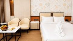 Premium Room view at Pride Premier Greater Noida showing a double bed, 2 armchairs with a coffee table, and a fruit platter.