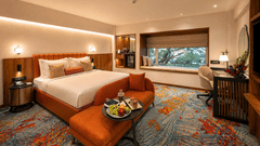 Elegant bedroom at Pride Premier Pune with a king size bed, cushioned bench and fruit platter on the table.
