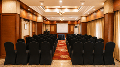 Conference hall with rows of black chairs and warm wood panelling at Pride Premier Pune, set up for events.