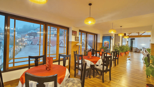 Orchid Restaurant at Central Heritage Resort and Spa, Darjeeling featuring several sets of table and chairs, plants across the dining space, and windows which provides outside view