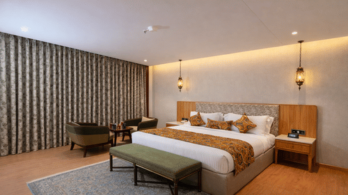 Bedroom of Superior Room with Bathtub furnished with a king size bed, a bench on a carpet, bedside tables, a seating area for 2, and 2 lights hung near the wall from the ceiling.
