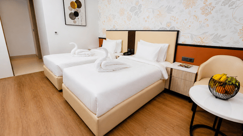 A Superior Twin Room featuring twin beds with towel swans, a bedside table, and a small round table with a fruit bowl at Pride Premier Greater Noida.