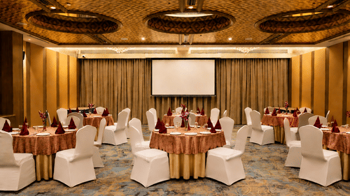Event hall at Pride Premier Pune with round table arrangements, stage area and decorative ceiling panels.