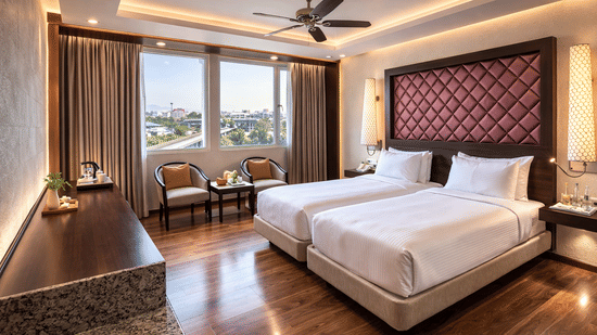 A room at Clarks Avadh, Lucknow, featuring twin beds, spreads, pillows, a television, and large windows.