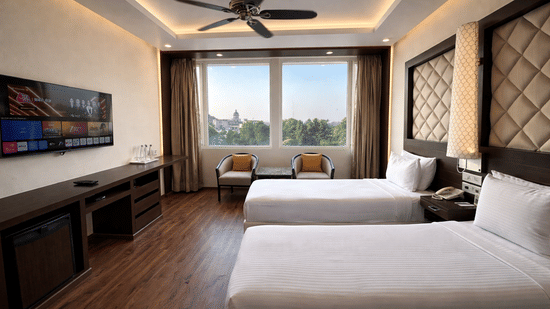A Superior Room Twin bed at Clarks Avadh, Lucknow, featuring twin beds, spreads, pillows, a television, and large windows.