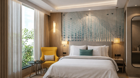 A well-lit guest room at KPG Sarovar Portico, Raj Nagar Extension, Ghaziabad, with a king size bed, an armchair by a large window, and 2 wall-mounted bedside lamps.