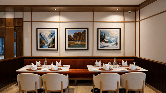 2 dining tables with 4 chairs placed in pairs on a side, and a sofa attached to the wall on which art pieces have been hung at Noor All-day Dining in Mountnoor Sarovar Premiere, Pahalgam.
