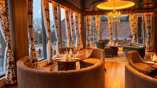 Seating tables and booths in Tamanna Kashmiri Speciality Lounge at Mountnoor Sarovar Premiere, Pahalgam, with round-shaped seating sofas, centre tables, and large glass windows offering views of the surroundings.