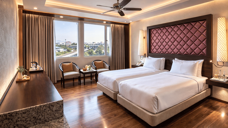 A room at Clarks Avadh, Lucknow, featuring twin beds, spreads, pillows, a television, and large windows.