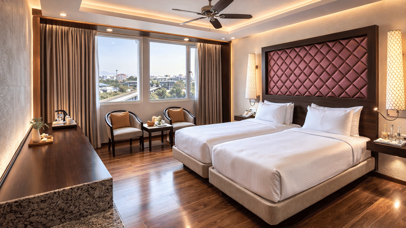 A room at Clarks Avadh, Lucknow, featuring twin beds, spreads, pillows, a television, and large windows.