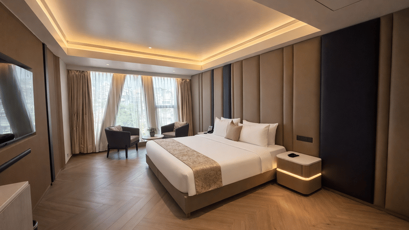 Premium room at Dragonfly Hotel – The Art Hotel with large bed, white linens, beige and brown accent pillows, wall paneling, pendant lights, seating area near window, and warm recessed lighting.
