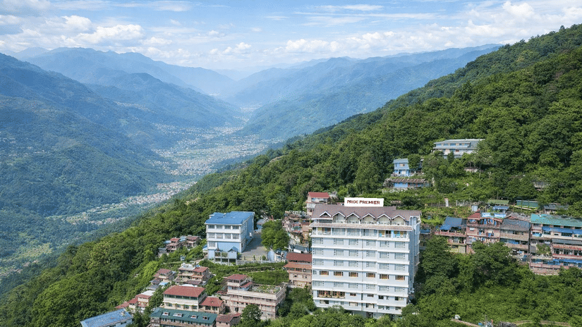 An aerial view of a hotel building nestled among forested mountains and a small town | Pride Premier Darjeeling