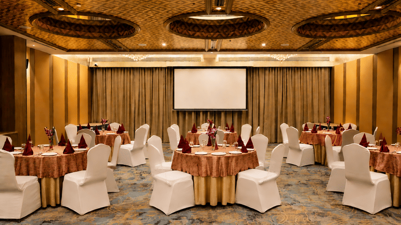 Event hall at Pride Premier Pune with round table arrangements, stage area and decorative ceiling panels.