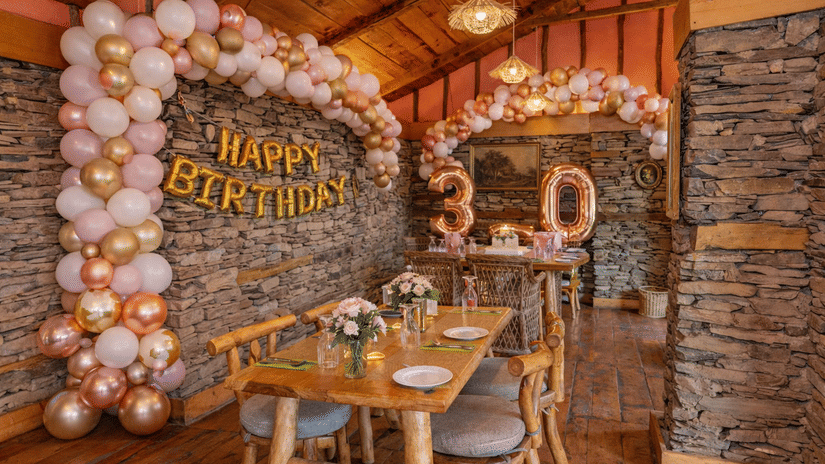 A rustic room decorated with pink and gold balloons and a Happy Birthday banner for a 30th birthday celebration - Manor Sports & Wellness Hotel