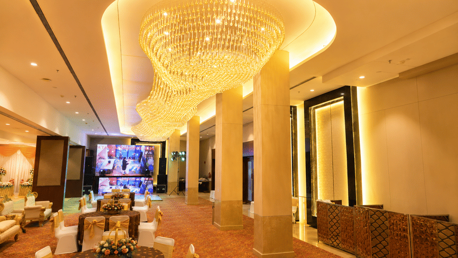 Grand banquet hall interior featuring a large ceiling chandelier, pillar lined seating area, and dining setup at Ambrosia Sarovar Portico, Haridwar.