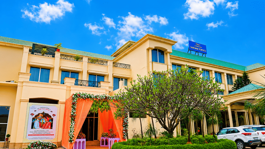 The facade of Ambrosia Sarovar Portico, Haridwar, with a landscaped driveway and entrance decor setup.
