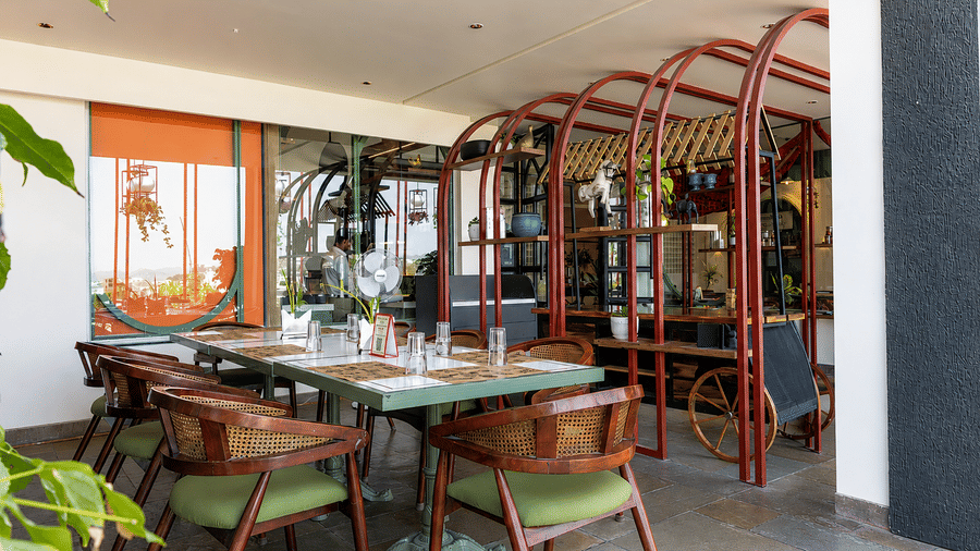 Covered outdoor dining area at Hotel Bawa, Udaipur with long dining tables, cushioned chairs, decorative metal archways, and wall decor.