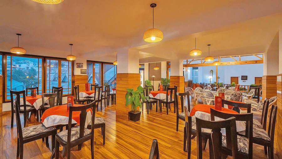 Orchid Restaurant at Central Heritage Resort and Spa, Darjeeling featuring ceiling lights, dining tables and chairs, and plants across the space.