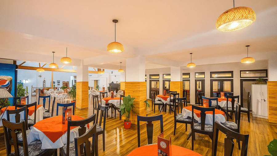 Orchid Restaurant at Central Heritage Resort and Spa, Darjeeling featuring several sets of dining table and chairs, and a ceiling light hanging from above