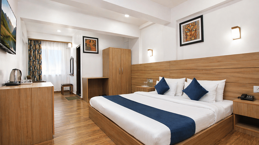 Front view of the Heritage Deluxe Non View room at Central Heritage Resort and Spa featuring a king bed with blue and white bedding wooden wall panels hardwood flooring and framed artwork.