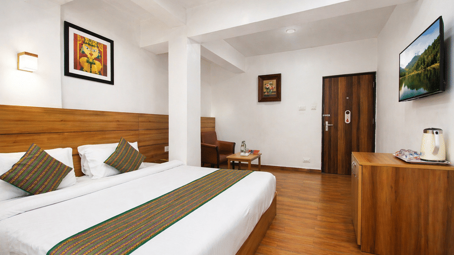 An alternate angle view of a room at Central Hotels showing a king bed with blue and white bedding wooden wall panels hardwood flooring framed artwork and wall-mounted TV near the door.