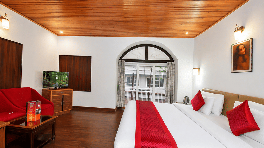 A room at Central Hotels featuring two beds with red bedding wooden ceiling a wall-mounted TV and large arched windows with a balcony view and warm ambient lighting.