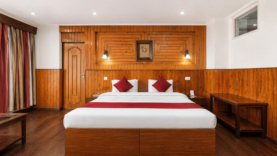 Front view of a room at Central Hotels featuring a king bed with red accent bedding wooden wall panels dark hardwood flooring warm wall lamps and red curtains on the window.