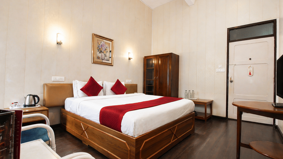 A cozy room at Central Hotels featuring a king bed with red and white bedding wooden furniture dark hardwood flooring a wardrobe and wall-mounted TV with natural light from above.