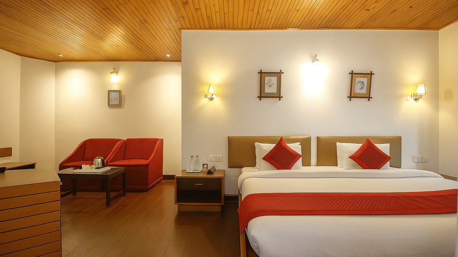 A triple bed room at Central Hotels featuring three beds with red and white bedding wooden ceiling warm wall lighting a sofa in the corner and dark hardwood flooring.