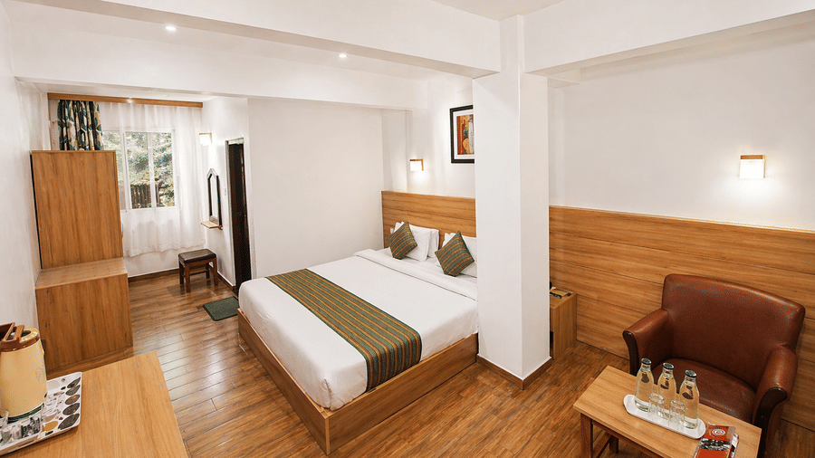 A twin bed room at Central Hotels featuring two single beds with white bedding wooden wall panels hardwood flooring a wooden wardrobe and a small seating area near the window.