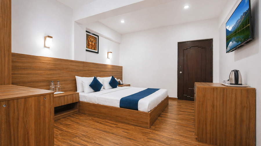 Wide angle view of a room at Central Hotels showing a king bed with blue accents wooden wall panels hardwood flooring framed artwork and a dark wooden door in the background.