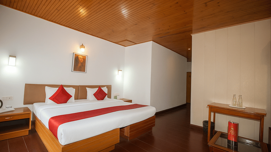 A room at Central Hotels featuring a king bed with red and white bedding wooden ceiling a work desk with chair wall lamps and dark hardwood flooring in a bright setting.