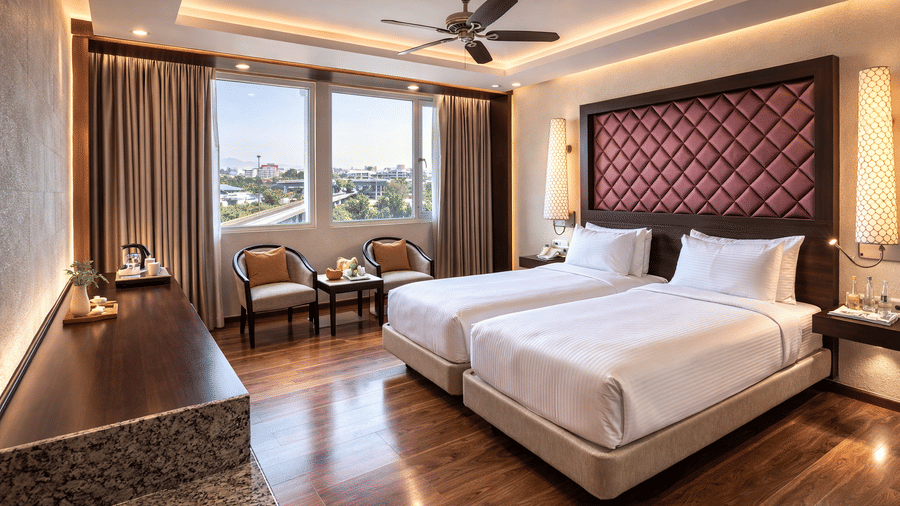 A room at Clarks Avadh, Lucknow, featuring twin beds, spreads, pillows, a television, and large windows.
