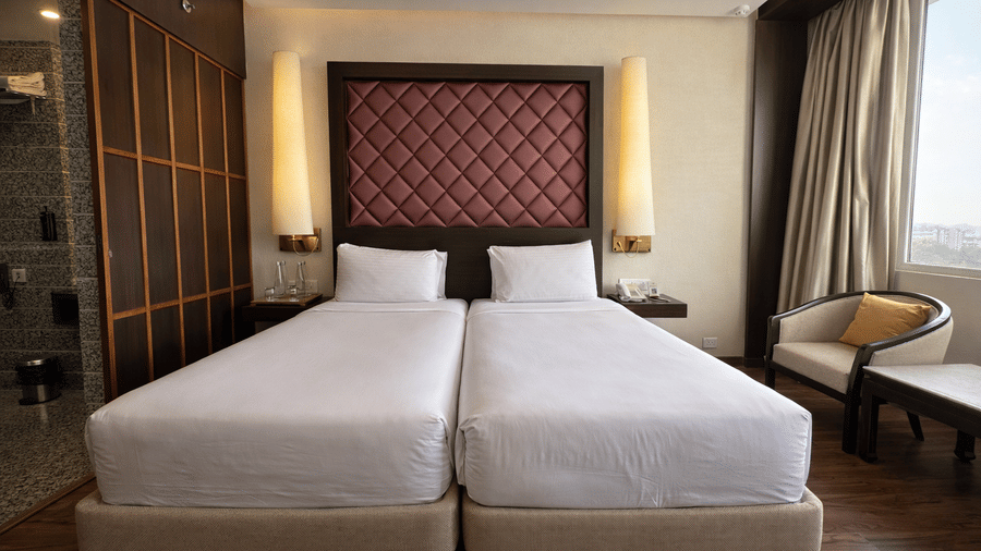 A room at Clarks Avadh, Lucknow, featuring twin beds, spreads, pillows,  and large windows.